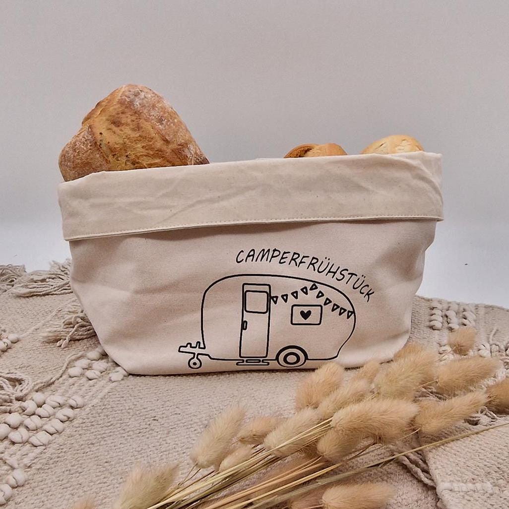 Schöner Naturfarbener Brotkorb aus Baumwollstoff, mit Aufgedrucktem Campingwagen und der Aufschrift Camper frühstück. der Druck kann leicht erfühlt werden, und ist einseitig. Die Obere Kante kann ja nach Inhalt umgeklappt werden. Er kann einfach zusammengefaltet und verstaut werden. Die Größe ist vergleichbar mit einem Mittleren Kochtopf.