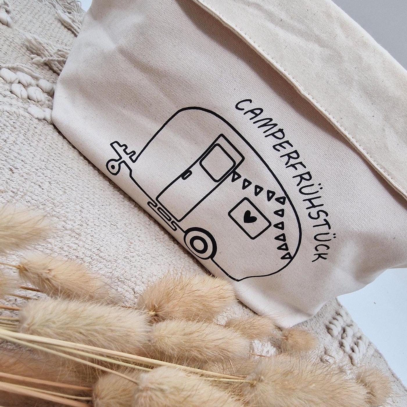 Schöner Naturfarbener Brotkorb aus Baumwollstoff, mit Aufgedrucktem Campingwagen und der Aufschrift Camper frühstück. der Druck kann leicht erfühlt werden, und ist einseitig. Die Obere Kante kann ja nach Inhalt umgeklappt werden. Er kann einfach zusammengefaltet und verstaut werden. Die Größe ist vergleichbar mit einem Mittleren Kochtopf.