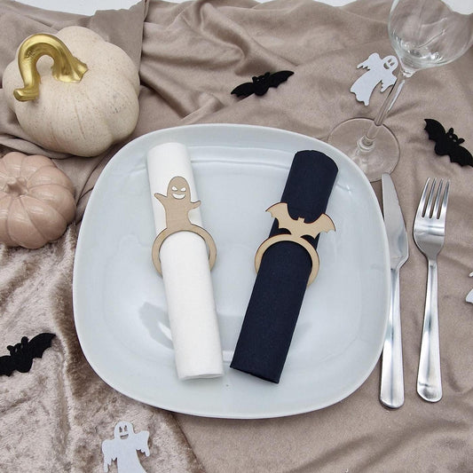 Zwei Holz-Serviettenringe mit Geist und Fledermaus auf weißer und schwarzer Serviette auf einem Teller als Halloween Tischdeko.