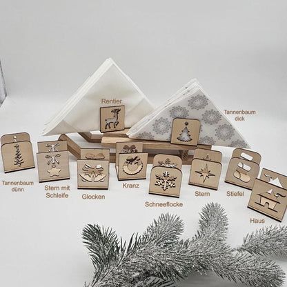 Alle Motive der handgefertigten Holz-Serviettenhalter im Überblick: Tannenbaum, Stern mit Schleife, Glocken, Kranz, Schneeflocke, Rentier, Stern, Stiefel und Haus – präsentiert mit Servietten und Tannenzweig auf hellem Untergrund.
