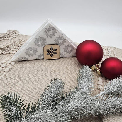 Handgefertigte Holz-Serviettenhalter mit weihnachtlichen Motiven wie Tannenbaum, Rentier und Stern – natürliche Tischdekoration auf beigem Untergrund mit Servietten und Tannenzweig.