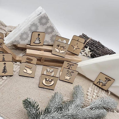 Set aus handgefertigten Holz-Serviettenhaltern mit verschiedenen Weihnachtsmotiven – Tannenbaum, Stern, Geschenk, Kranz und Rentier – auf beiger Tischdecke mit Servietten und Tannenzweig arrangiert.