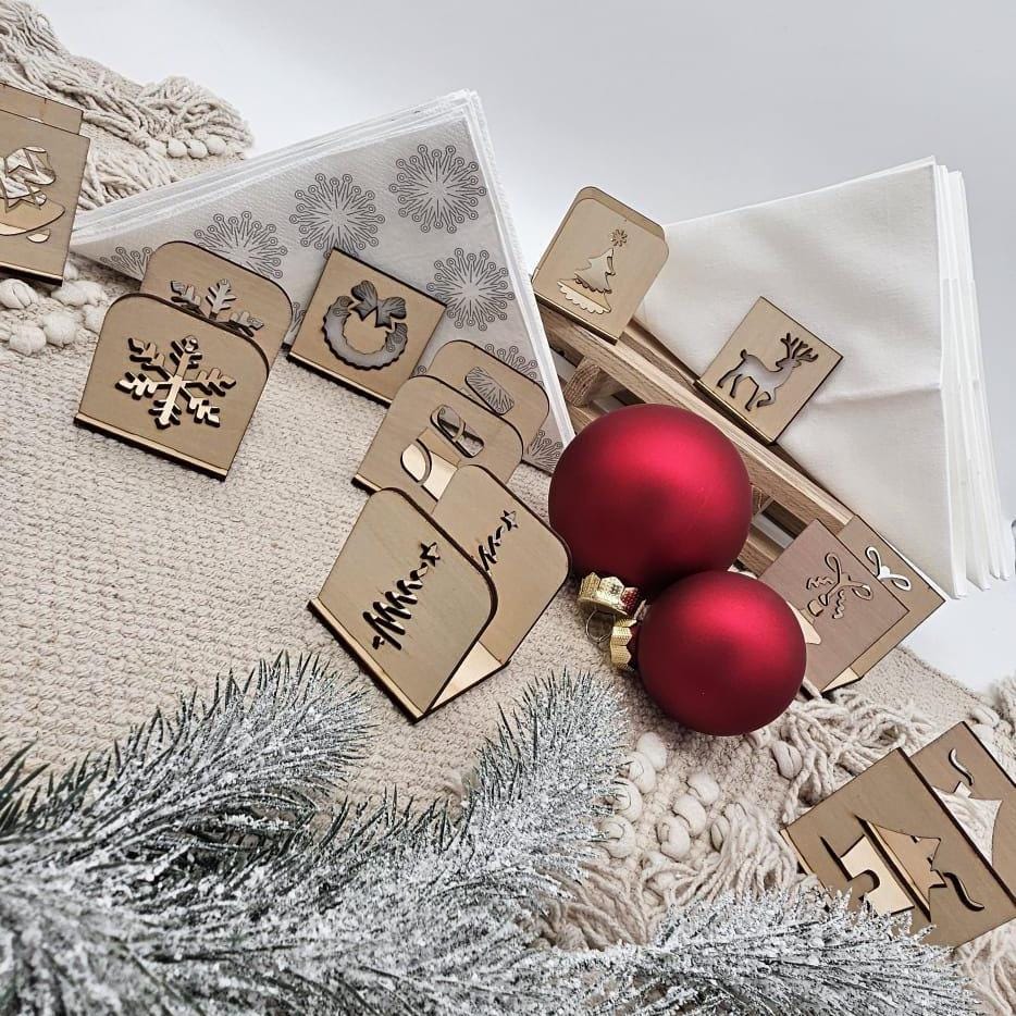Verschiedene weihnachtliche Serviettenhalter aus Holz mit Motiven wie Schneeflocke, Tannenbaum und Rentier vor weiß geschmückten Servietten und roten Weihnachtskugeln.
