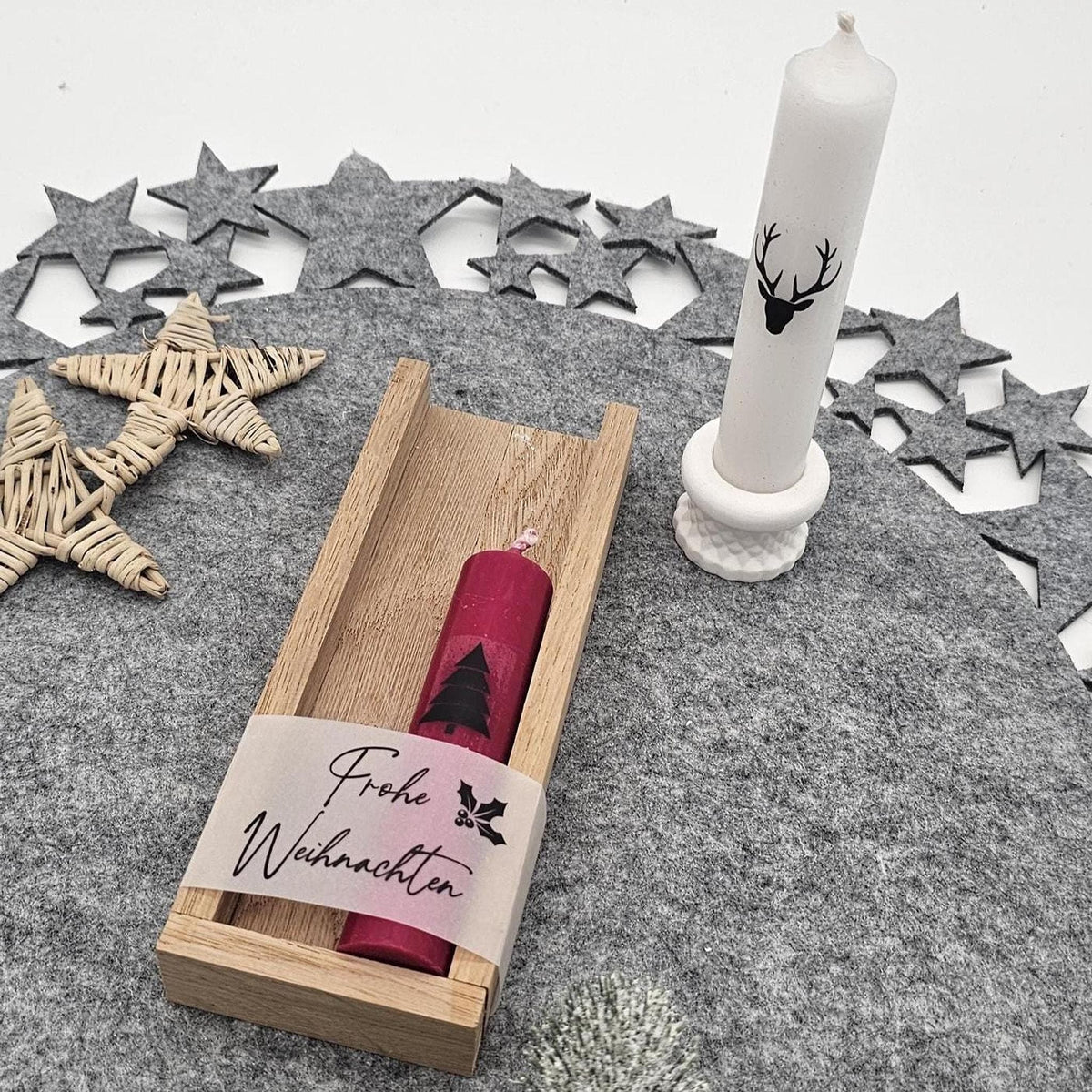 Weihnachtliches Geschenkset: Rote Kerze im Holztablett mit der Aufschrift ‚Frohe Weihnachten‘ und weiße Stabkerze im Ständer.