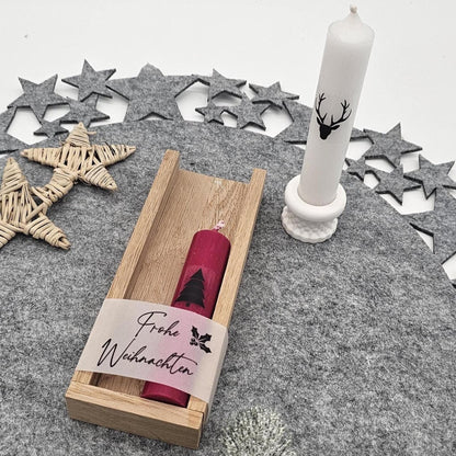 Weihnachtliches Geschenkset: Rote Kerze im Holztablett mit der Aufschrift ‚Frohe Weihnachten‘ und weiße Stabkerze im Ständer.