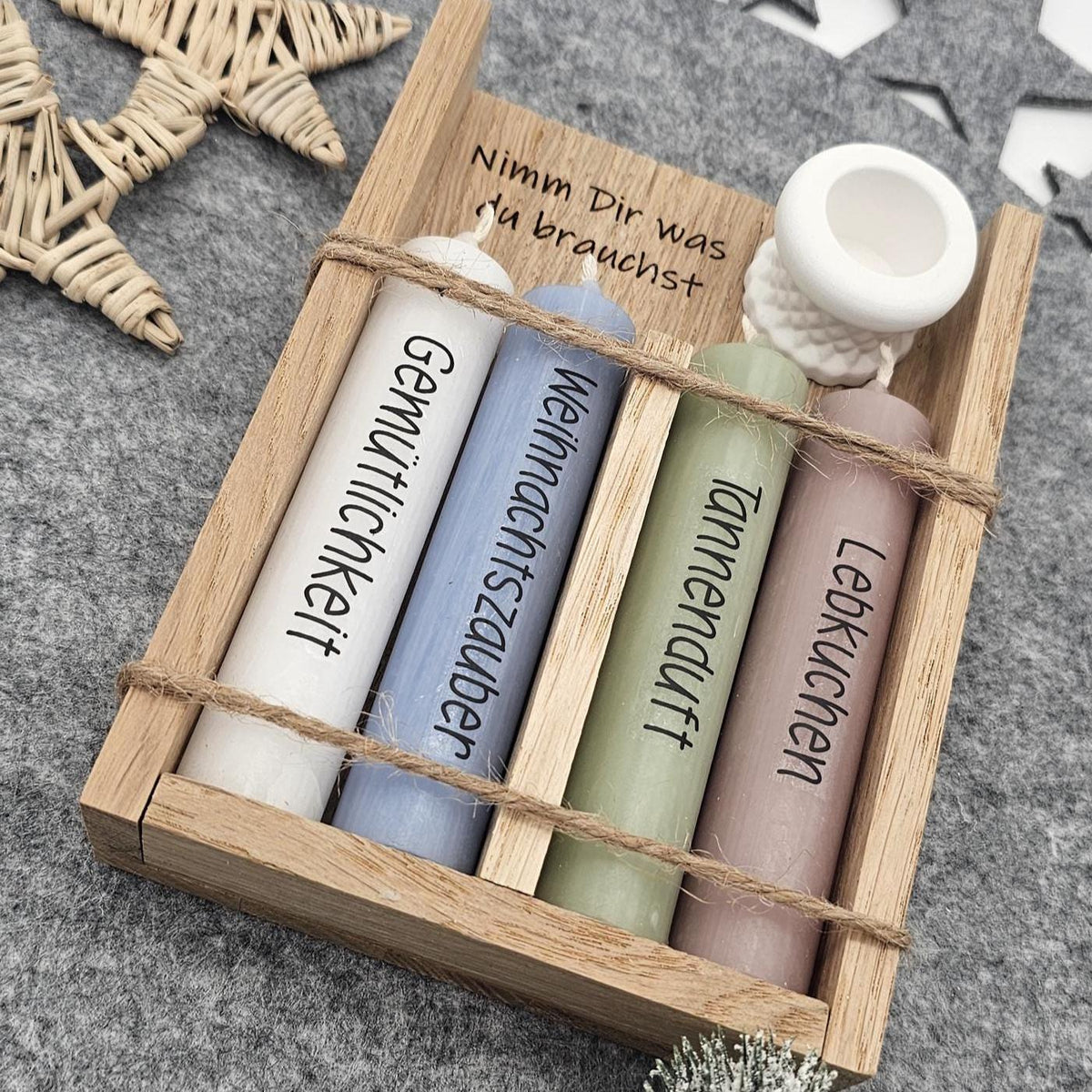 Detailreiche Nahaufnahme: Weihnachtsgeschenkset in Holzbox mit Gravur ‚Nimm Dir was du brauchst‘, vier Stabkerzen mit Aufschrift Gemütlichkeit, Weihnachtszauber, Tannenduft, Lebkuchen und weißem Kerzenständer.