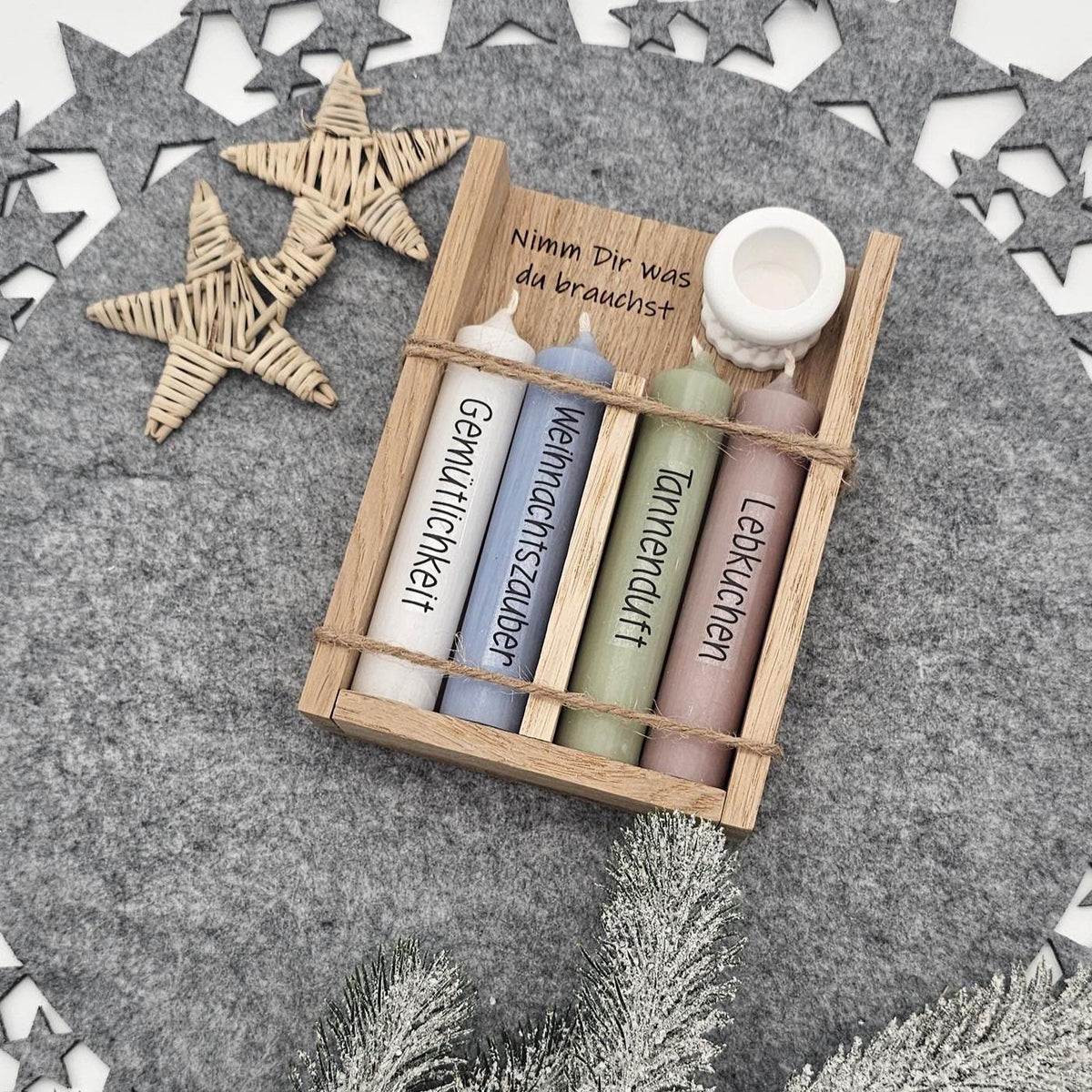 Weihnachtsgeschenkset in Holzbox mit Gravur ‚Nimm Dir was du brauchst‘: Vier bunte Stabkerzen mit Aufschrift Gemütlichkeit, Weihnachtszauber, Tannenduft, Lebkuchen und weißer Kerzenständer auf Filzunterlage.