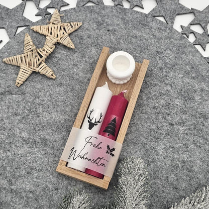 Handgemachtes Weihnachtsgeschenk-Set in Holzbox: Enthält eine weiße Stabkerze mit Hirsch, eine rote Motivkerze mit Tannenbaum und „Frohe Weihnachten“-Banderole sowie einen weißen Kerzenhalter auf weihnachtlich dekoriertem Filz.